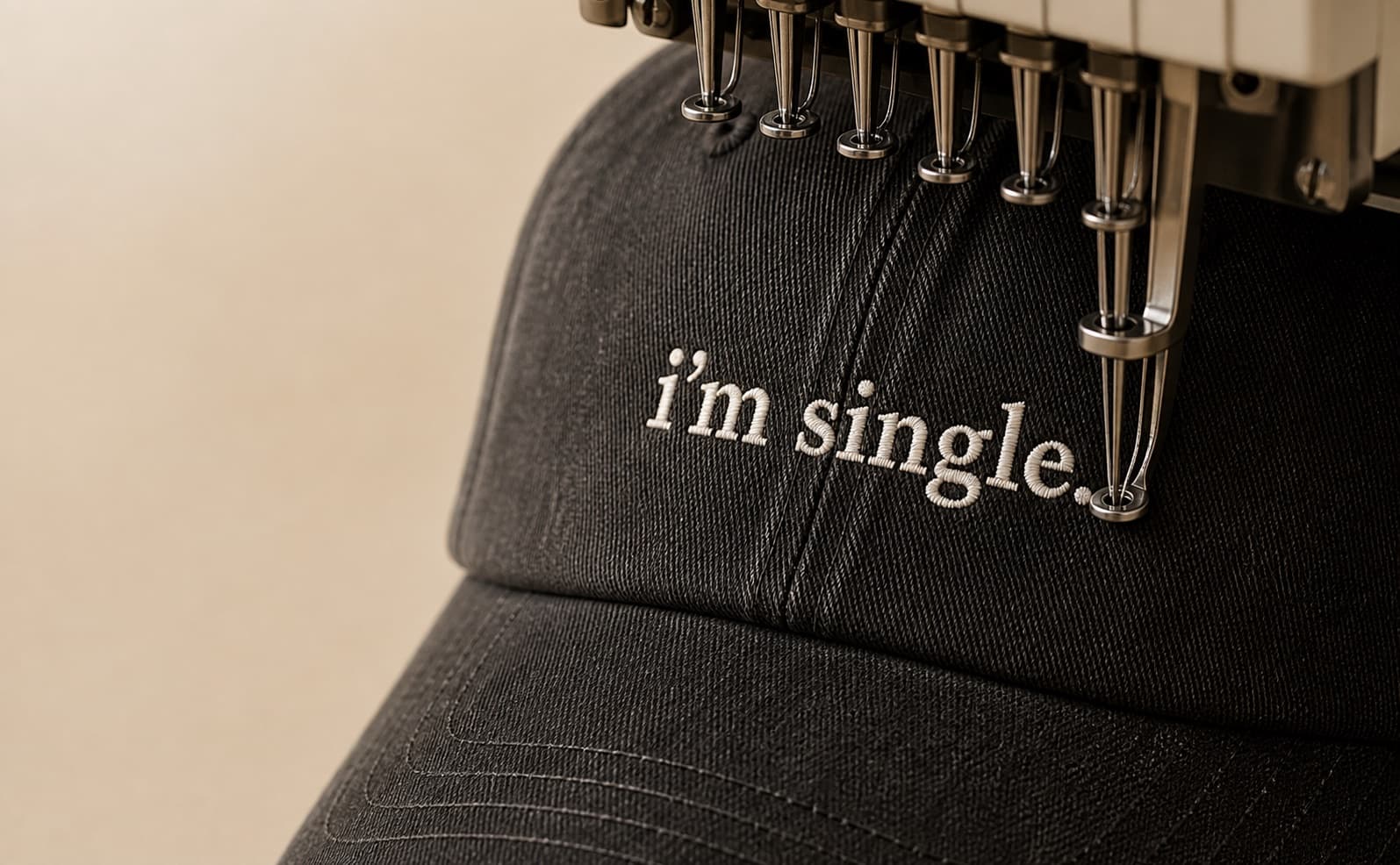 an embroidery machine stitching “i’m single.” into a washed black cap